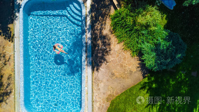 空中无人驾驶飞机观看游泳池中的小女孩从上面的孩子游泳在充气环多纳儿童在家庭度假胜地的蓝色水中玩