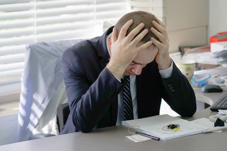 男医院秘书坐在她的工作场所. 健康问题压力和抑郁. 男性用手抱着头.