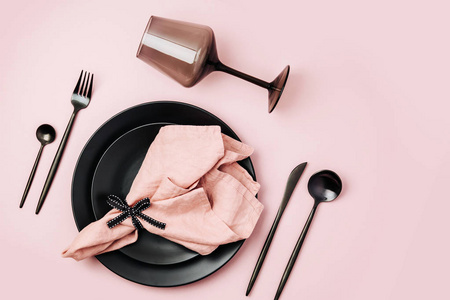 节日餐桌设置与餐具，淡粉色餐巾，黑色盘子和酒杯在糊状背景。 平躺式顶部视图