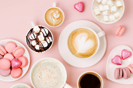 各种不同大小的杯子里的咖啡，在淡粉色的背景上有糖果和马卡龙。 咖啡时间概念。 平躺式顶部视图