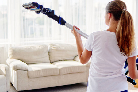 特写年轻女子穿着白色衬衫，手里拿着无线吸尘器，一边在客厅打扫，在家里的后景复制空间。 家务清洁和家务观念