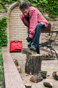一个穿着红色格子衬衫的人正在用一把刀锯用一个结锯一根木头。腿把圆木压到树桩上
