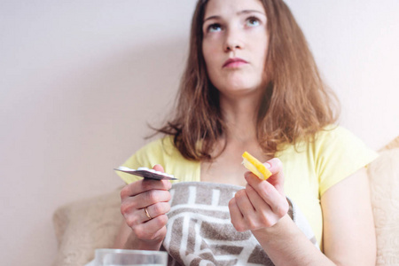 感冒的女人在药片和维生素之间选择治疗。 冬季季节性流感