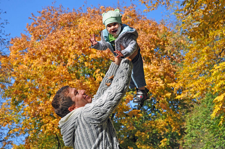 微笑的父亲和他笑的孩子在阳光明媚的秋天公园散步，玩得很开心