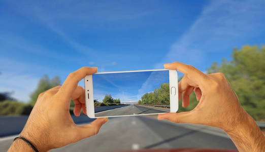 驾驶和电话的概念。 手拿着智能手机在模糊沥青道路背景上拍照。 三维插图