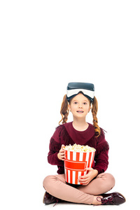 头上戴虚拟现实耳机的孩子，手上拿着白色的条纹爆米花桶