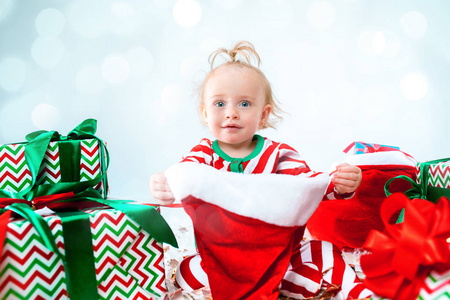 可爱的女婴 1岁, 戴着圣诞老人的帽子摆姿势在圣诞节的背景。带着圣诞舞会坐在地板上。节日