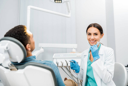开朗的牙医拿着钻，微笑着靠近非裔美国人病人