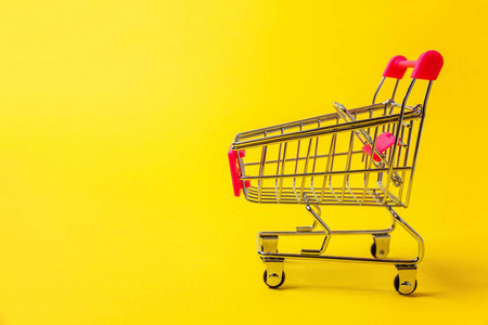 小超市杂货店推车购物玩具与车轮隔离在黄色五颜六色的现代时尚背景。 销售购买商场市场商店消费者概念。 复制空间