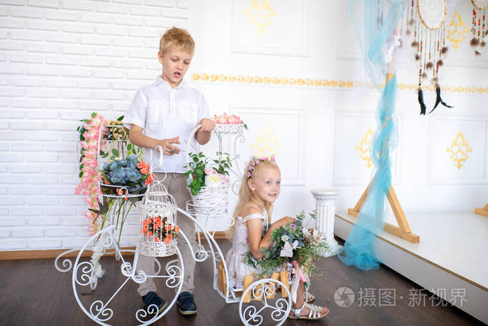 白色房间里的儿子和女儿正在为可爱的母亲准备一个惊喜。 装饰花，花店花束。 祝贺三月八日或送给心爱的木乃伊的生日礼物。 生活方式