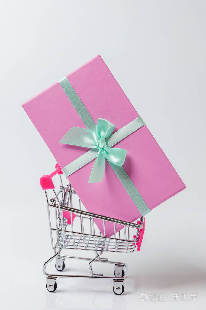 小超市杂货店推车购物玩具与粉红色礼品盒隔离在白色背景。 销售购买商场市场商店消费者概念。 复制空间