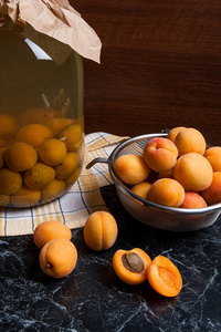 成熟的有机杏子在夏季收获，大玻璃罐与罐装甜杏组成的深色大理石。 有机黄多汁杏子整体成分，钢卷和自制杏子成分减半，b罐装