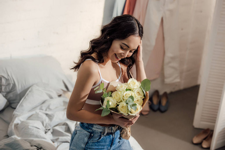 美丽快乐的年轻亚洲女人在卧室里捧着一束白玫瑰