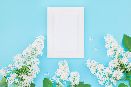 创意平躺概念顶部视图空白明信片框架模拟和白色丁香花花瓣在粘贴蓝色背景与复制空间在最小风格模板的文字或设计