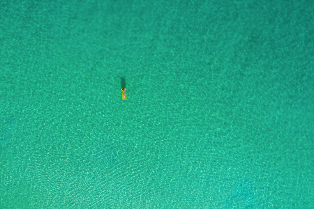 鸟瞰苗条的女人在塞舌尔透明的绿松石海的游泳床垫上游泳。 夏天海景与女孩美丽的波浪，五颜六色的水。 无人驾驶飞机的俯视图