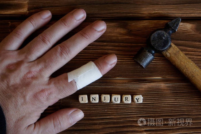 接合者受伤的手。 锤子在手指上。 木工作业中的伤害。 木制背景上的字母。