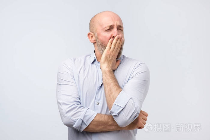 的成熟男人在辛苦工作了一天后打哈欠,用灰色背景上孤立的手闭上嘴