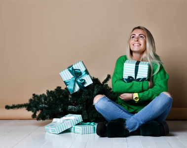 年轻女子坐在冷杉圣诞树附近的地板上, 梦想着在这个圣诞节的夜晚, 现在未来礼物和等待奇迹的到来