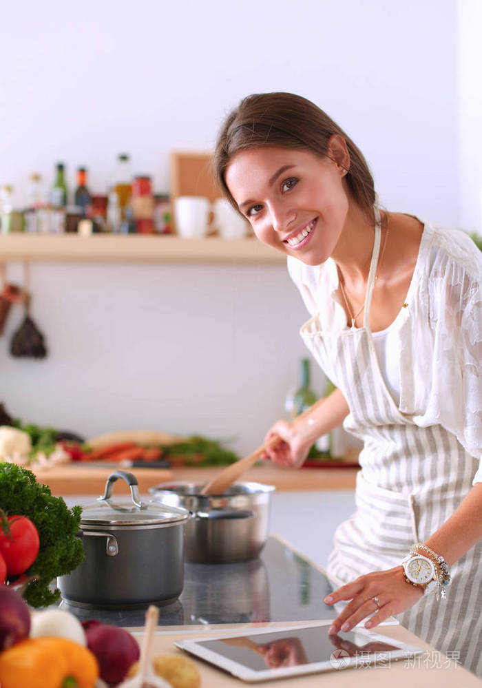 使用一台平板电脑,在她的厨房里做饭的年轻女人