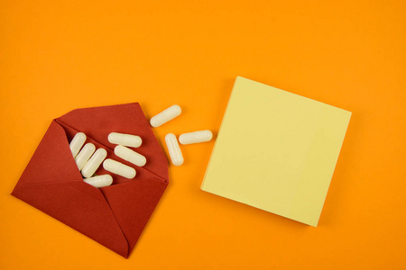 红色信封中的白色药丸和橙色背景中的黄色棍子笔记