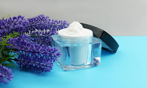 一个蓝色背景的淡紫色花，装在玻璃罐子里的奶油，用于面部和手部护理