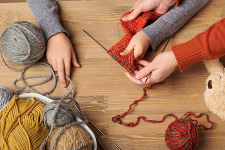 女孩子正在学习编织。 五颜六色的羊毛纱线在木桌上。 手特写。