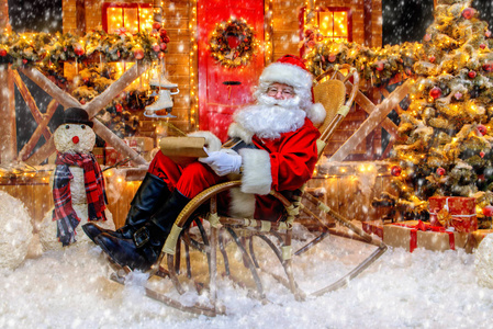 圣诞老人坐在摇椅上,正在他的房子附近写信,里面装饰着圣诞灯.