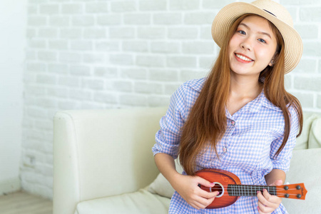 亚洲年轻女子，头发秃顶，学习在砖块背景上演奏四弦琴，她唱着一首快乐有趣和微笑的歌。