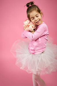 可爱的小女孩在薄纱裙与粉红色的背景上的花束的鲜花
