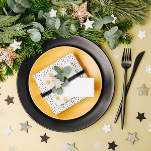 节日餐桌设置。 带有礼物的黑色盘子和带有杉树枝的圣诞装饰品。 平躺顶部视图。