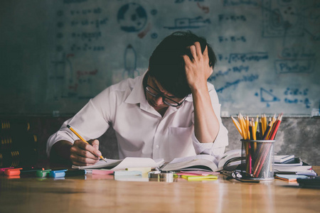 年轻的亚洲学生男子坐在办公桌前在家学习和阅读，做家庭作业和课程实践，准备考试，以进入教育概念。