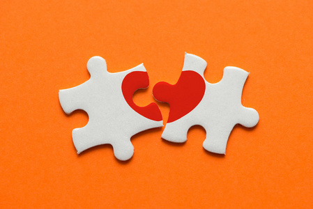 拼图diy特写两块拼图与红色心脏在橙色背景.照片
