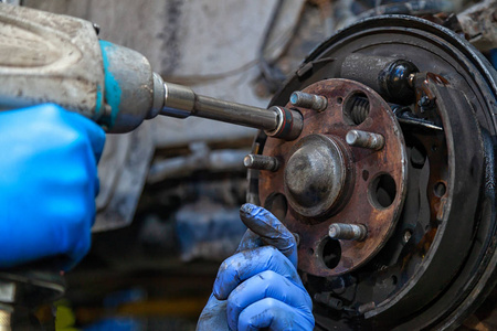 关闭更换旧的前制动盘制动卡尺和轮毂螺母在一辆汽车用气动扳手在电梯上抬起。 汽车修理工。