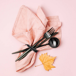 黑色餐具，淡粉色餐巾纸和秋叶在糊状背景上。 平躺式顶部视图