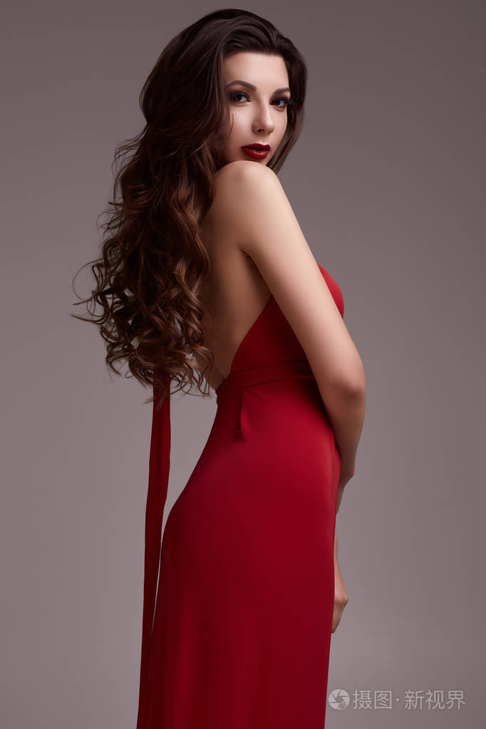 美丽的年轻性感的黑发女人的肖像,卷发,穿着红色连衣裙,在演播室背景