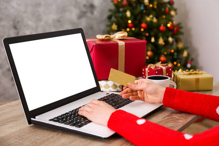 女性手与黄金信用卡笔记本电脑圣诞礼物装饰树的背景。 女人在网上挑选礼物，在她的笔记本电脑上购物。 木桌复制空间关闭。
