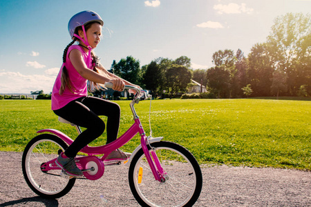 戴头盔骑自行车的女孩。夏季公园的自行车手