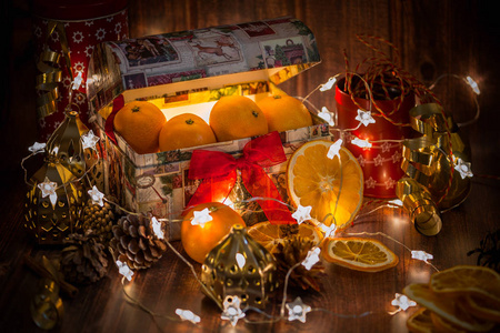 圣诞装饰附近装满橘子的圣诞盒，浅星花环，干橘子，木制背景，深色主题