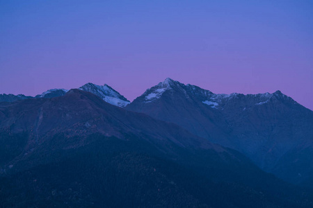 夕阳下的群山。 紫色的山峰和深蓝色的天空。雪山