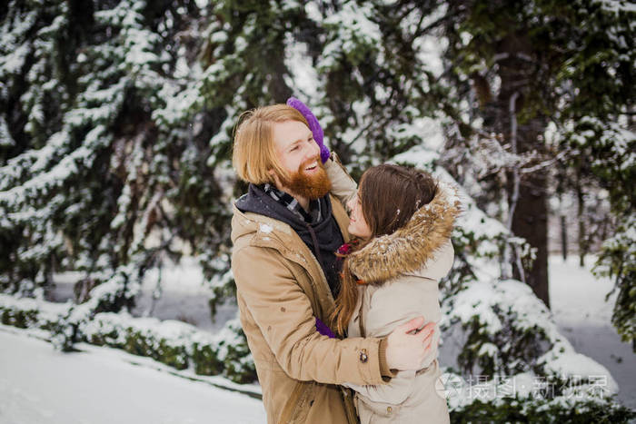 一个留着胡子的白种人男孩和一个女孩在冬天公园的户外约会，背景是一棵下雪的针叶树，玩雪球，扔雪挂自己，玩冬天的游戏。