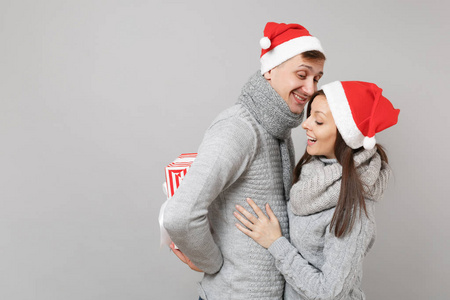 快乐有趣的夫妇女孩男子红色圣诞帽灰色毛衣围巾隔离在灰色墙壁背景工作室肖像。 新年快乐，2019年庆祝节日聚会的理念。 模拟复制空