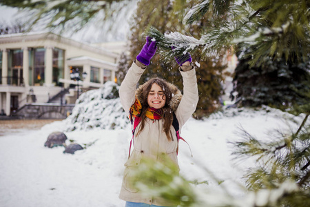 美丽的年轻白种人女人快乐幸福幸福，微笑雪附近的针叶树在一个下雪的公园。