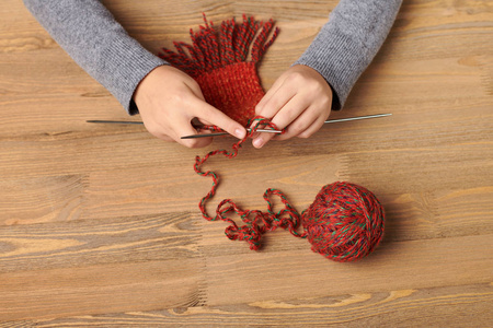 女孩子正在学习织围巾. 红色羊毛纱在木桌上. 手特写.照片