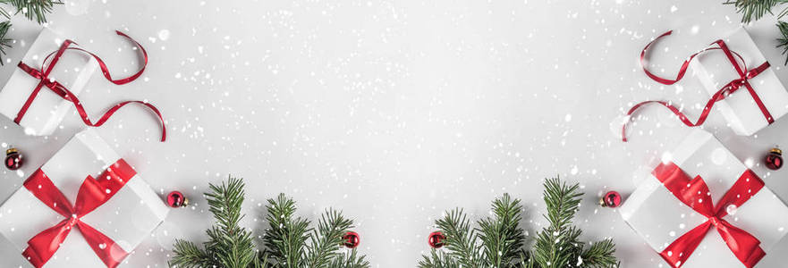 创意框架由圣诞杉木树枝在白纸背景上与红色装饰礼品盒。 圣诞节和新年主题。 平躺式顶部视图