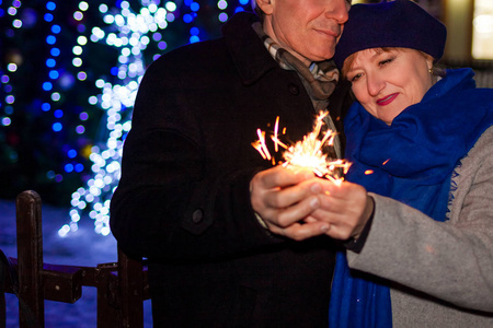 高级家庭夫妇在晚上通过假日照明燃烧火花。 圣诞节和新年概念