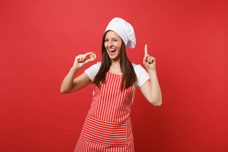 家庭主妇女厨师或面包师穿条纹围裙，白色T恤，烤厨师帽子隔离在红墙背景上。 微笑的女人持有比特币比特币未来货币。 模拟复制空间概念