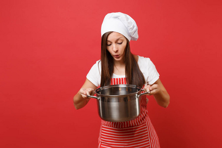 家庭主妇女厨师或面包师穿条纹围裙，白色T恤，烤厨师帽子隔离在红墙背景上。 美丽的管家女人拿着空的陶器罐。 模拟复制空间概念