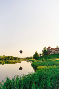 在大自然中膨胀。 美丽的热气球飞在城堡附近的湖面上。