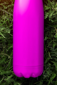 不锈热水瓶水瓶粉红色。 模型隔离在绿草背景上，具有阳光效应。 有光泽的铝真空热倒瓶