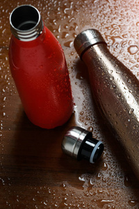 两个不锈钢热瓶在一张木桌上喷水。 阳光效应
